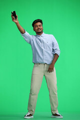 A man in a blue shirt, on a green background, in full height, waving his phone