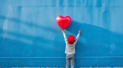 Photo sur Plexiglas Ballon Rear view of a kid raising arms with red heart shaped balloon on blue background