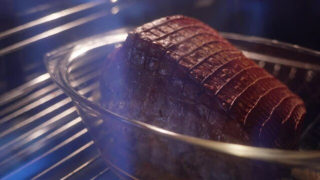 a large piece of pork in the oven in a net, in a transparent container, is baked in the oven at high temperature. juice squeaks on the meat
