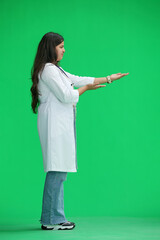 A female doctor, on a green background, in full height, points to the side, profile