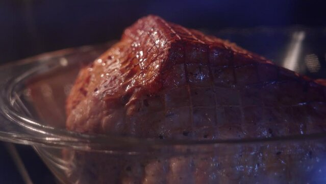 A large piece of pork in the oven in a transparent container is baked in the oven at high temperature. juice squeaks on the meat