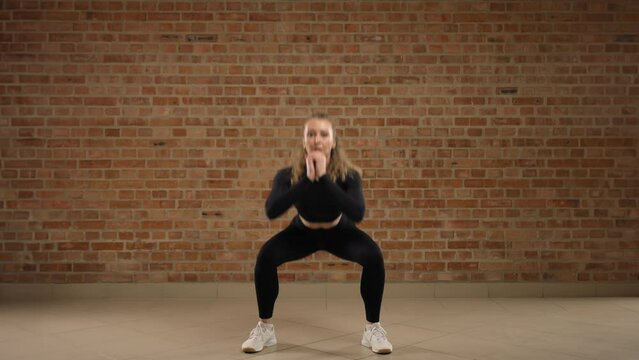 A trainer diligently demonstrates how to properly perform squat pulses. She is exercising in a seamless loft gym, embracing sports and a healthy lifestyle. RED V-RAPTOR 8K RAW.