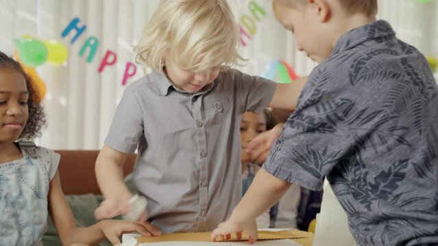 Excited boy opening birthday present with watching friends