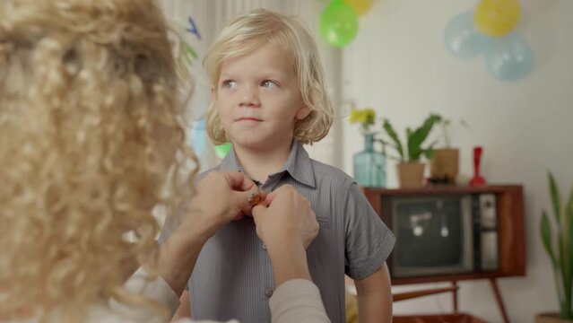 Mother buttoning shirt of son before his birthday party