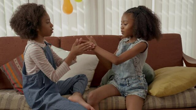 Cute girls sitting on sofa playing clapping game