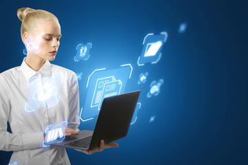 Attractive blonde businesswoman using laptop with glowing blue icons on blurry background. Online management and remote work concept.