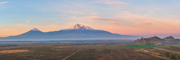 Wide angle panoramic view of sunrise over the Ararat mountains with vineyards and old Khor Virap monastery at fall. Travel destination Armenia