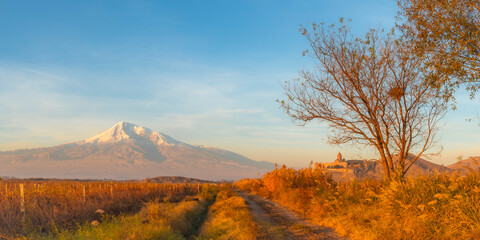 Wide angle panoramic view of sunrise over Ararat mountains, vineyard field, fruit trees, and ancient Khor Virap monastery at fall. Travel destination Armenia