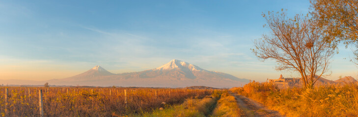 Super wide angle panoramic view of sunrise over Ararat mountains, vineyard field, fruit trees, and ancient Khor Virap monastery at fall. Travel destination Armenia