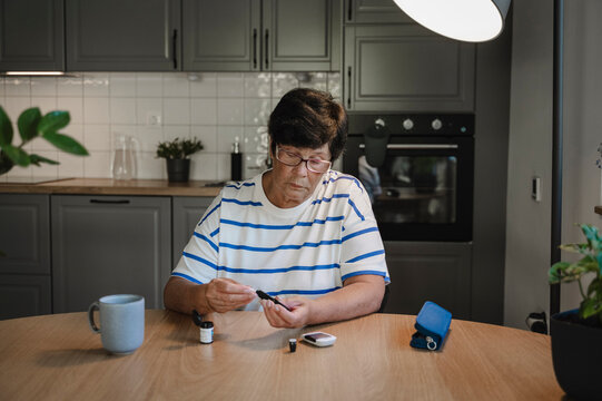 Senior Woman Measuring Blood Sugar With Glucometer At Home