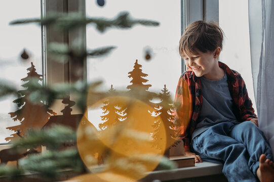Smiling boy admiring Christmas decoration near window at home