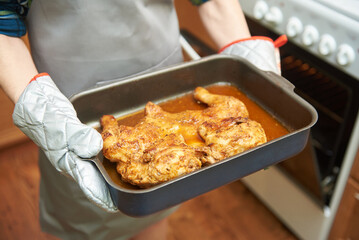 The female hands holds a cooked chicken from the oven