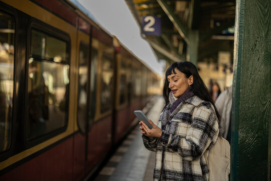 Woman using smart phone standing by train arriving on platform