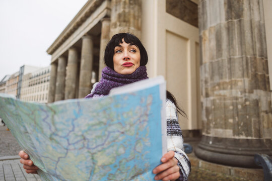 Contemplative woman with map standing on footpath