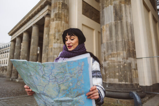 Woman examining map standing on footpath in front of building