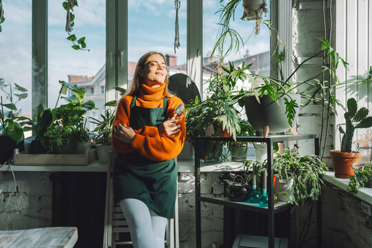 Smiling botanist with eyes closed leaning on window sill in plant store