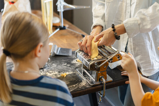 Woman cutting dough in pasta maker with son and daughter at home