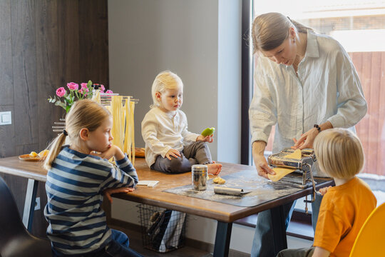 Woman cutting dough in pasta maker with family sitting at dining table