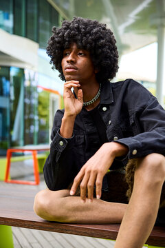 Non-binary person with curly hair sitting on bench