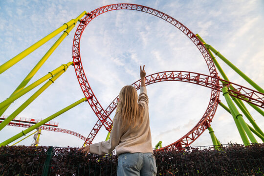 Young woman gesturing peace sign in front of rollercoaster