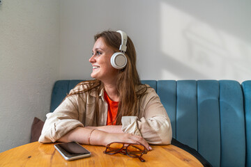 Smiling young woman wearing wireless headphones and sitting in cafe