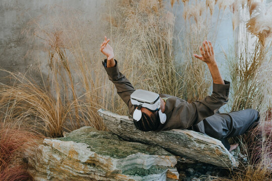 Businessman gesturing with virtual reality simulator and lying on rock in garden