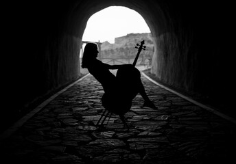 Silhouette of a woman in a tunnel, sitting balanced on a chair while holding a cello
