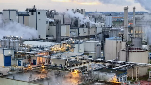 Drone footage captures a sprawling factory with chimneys emitting smoke, yellow lights highlighting its industrial nature.