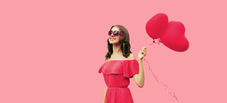 Portrait of happy smiling young woman holding pink heart shaped balloon on studio background