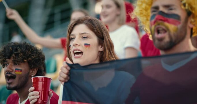 Lovely couple supporting their national team by yelling and singing something from stadium tribunes. Supporting team at sports event. Covering face with paint of German national team.