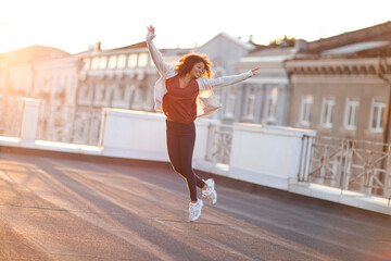 Full-length of young carefree african american woman jumping at rooftop in morning sunlight