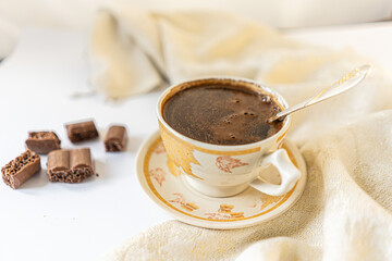 Cup of coffee with chocolate on a light white table and beige napkin. Breakfast coffee in bed
