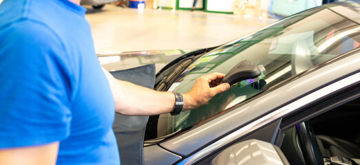 Mechanics man changing the broken windshield and automobile windshield or windscreen replacement of white car in Auto Repair Shop