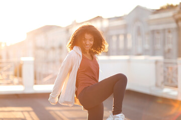 Young happy sporty african american woman doing sport exercising on roof and smiling at camera