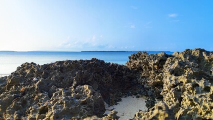 a circular rock in the middle of white sand on the edge of the coastline with a view of the turquoise sea