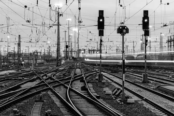 Türaufkleber Railway infrastructure at Frankfurt main station, Germany. Black and white panorama. Technology with signals, crossings, catenary, tracks, switches at twilight. Blurred fast train lights in motion.  © ON-Photography