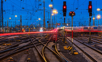 Blue hour at the main station of Frankfurt Main Germany with railway infrastructure technology, signals, crossings, catenary, glistening tracks, switches at twilight. Blurred train lights in motion. 