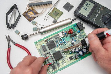 Close-up of a technician's hands in a workshop. The repairer is soldering an IC in a PLCC package to the circuit board of an electronic device.