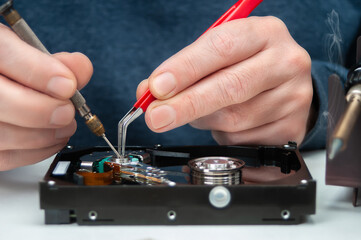 Close-up of a technician's hands in a workshop. The technician is using tweezers and a screwdriver...