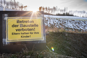 Gelbes, dreckiges  Baustellenschild im Sonnenlicht vor verschneitem Hintergrund mit dem Hinweis...