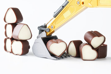 Toy excavator bucket with heart-shaped chocolates. Concept of mining and choosing a love partner,...