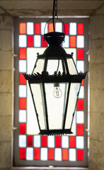 ceiling lamp in iron, in front of the window with glass and stained glass of red squares.