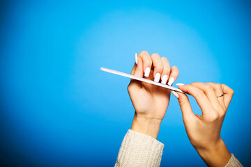 Crop woman filing long nails on blue backdrop