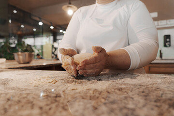 Crop anonymous female cook in white uniform kneading dough making ball on marble counter in restaurant kitchen
