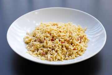 Cooked brown rice in white plate on dark background.