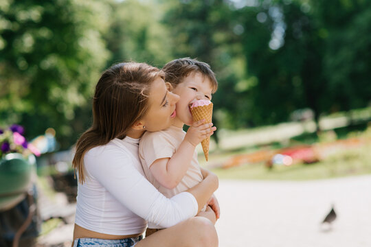 Young Caucasian mother with a little boy eating ice cream outdoors. Summer food and free time