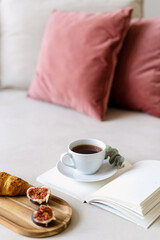 Selective focus on cup with coffee, notebook and wooden tray with breakfast on armchair