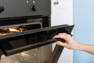 Woman hand open door of electric oven for prepare dinner at kitchen