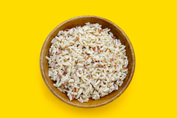 Cooked brown rice in wooden bowl on yellow background.