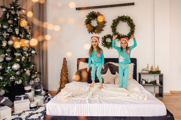 Cute twins in pajamas and santa hats jumping on bed